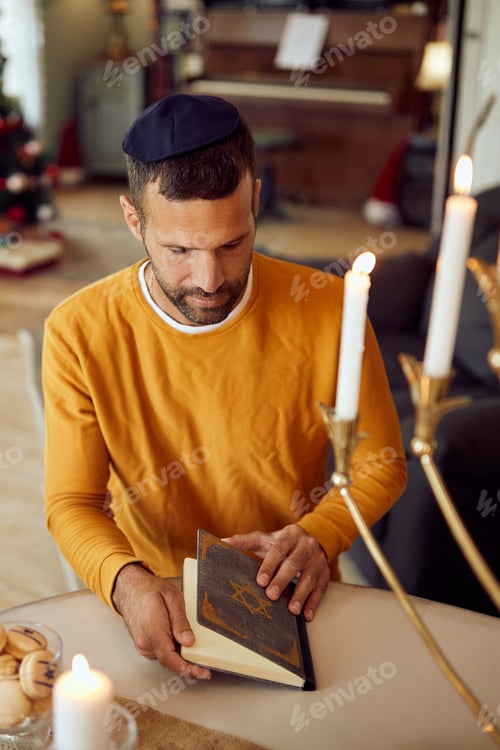 Preview: Mid adult man reading Hebrew bible during Jewish holiday, Hanukkah at home.