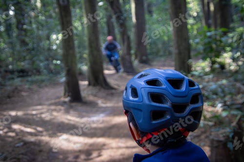 Preview: Rear view of a boy cycling in the forest wearing a helmet