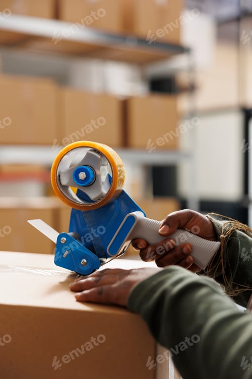 Preview: Cheerful employee using adhesive tape to pack cardboard box