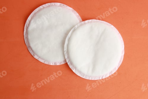 Preview: Flat lay of white absorbent nursing pads on an orange background