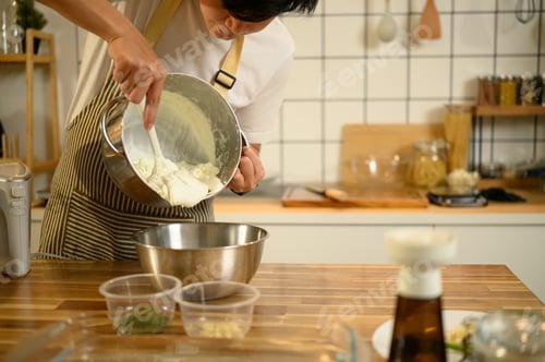 Preview: Smiling asian man wearing an apron preparing whipped cream in cozy kitchen