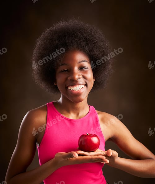 Preview: young ethnic woman with afro hairstyle happy with an apple in her heart