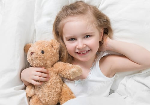 Preview: Girl holding her brown teddy, in bed