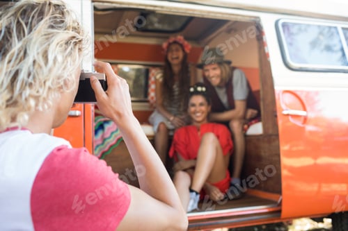 Preview: Man photographing happy friends sitting in camper van