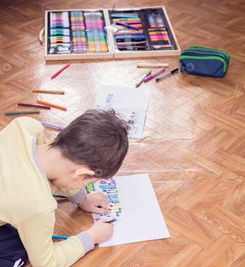 Preview: The child boy sits on the floor and draws a picture with colored markers on white sheet.
