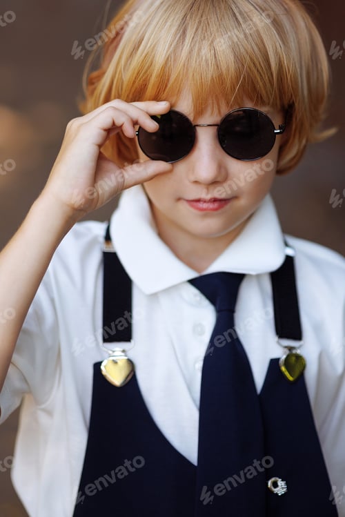 Preview: Portrait of a young schoolgirl in black round sunglasses and school uniform. Back to school.