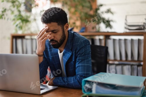 Preview: Young exhausted male employee in front of notebook in his office.