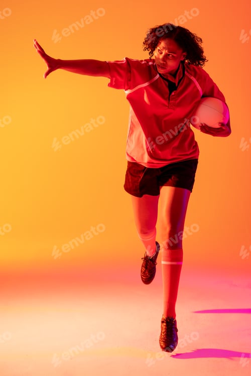 Preview: African american female rugby player with arm wide and rugby ball over neon pink lighting