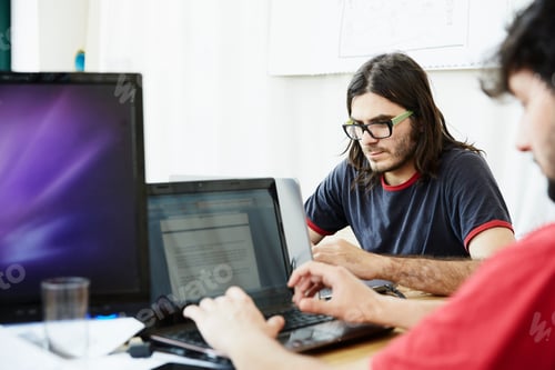 Preview: Focused coworkers working on laptops in a modern office space.