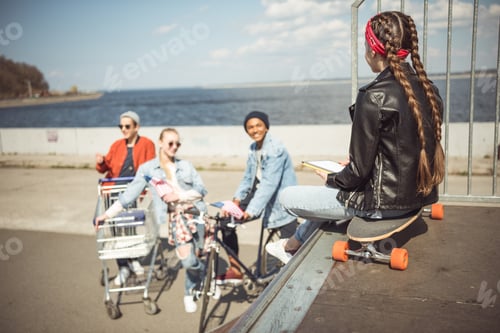 Preview: rear view of teenager girl using digital tablet and sitting on skateboard in skateboard park,
