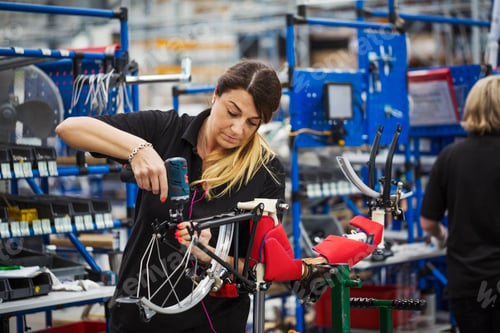Preview: Female skilled factory worker assembling a bicycle in a factory working on the frame and wheels.