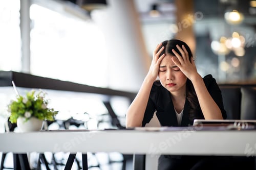 Preview: Shot of Asian young businesswoman looking stressed while sitting in her office in front of the lapto