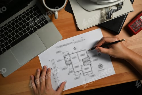 Preview: Architects man working on construction plans and using laptop on wooden desk.