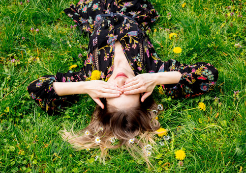 Preview: Young woman lying down on green dandelion meadow