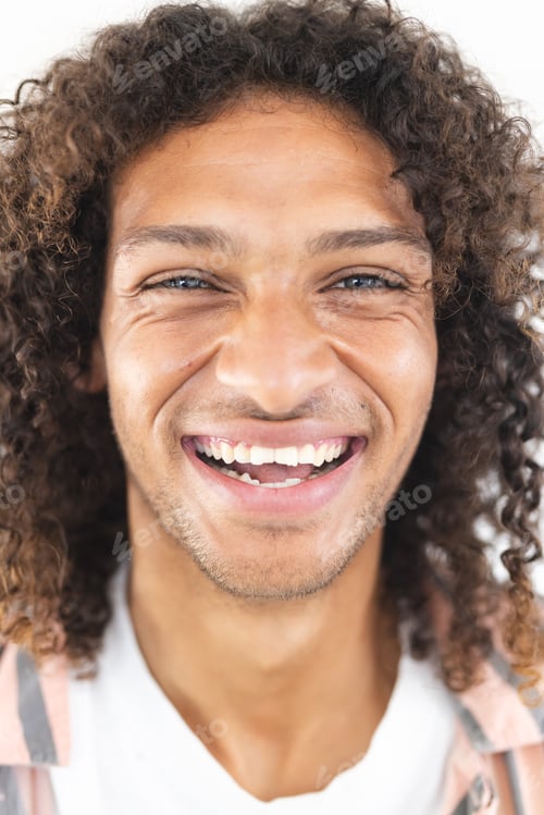 Preview: Young biracial man with curly hair smiles broadly, showcasing joy