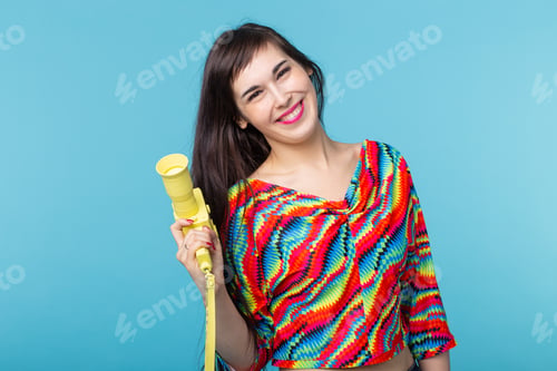 Preview: Portrait of a smiling young woman with a vintage yellow video camera in her hands posing against a
