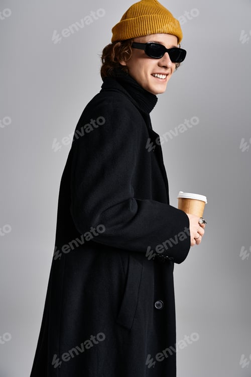 Preview: A stylish young man in a yellow beanie and black coat poses confidently in a studio