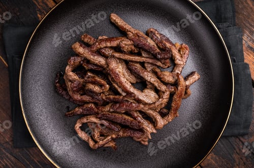 Preview: BBQ Fried beef tender strips, sliced steak in a plate. wooden background. top view