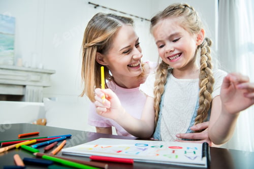 Preview: Happy mother and daughter hugging while drawing together at home