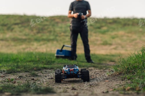 Vista previa: Focus on remote control car in nature with man in blurry background.