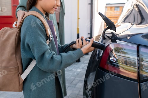 Preview: Adorable girl with backpack helping to charge electric car