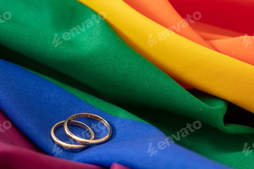 Preview: LGBT Gay marriage. Pair of golden rings on rainbow color textile, close up view. Copy space