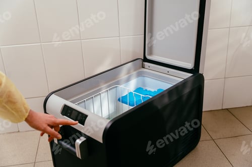 Preview: Person adjusts settings on open medical freezer with ice packs inside.