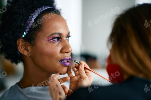Preview: Mid adult black woman woman putting on make-up for Mardi Gras festival celebration.
