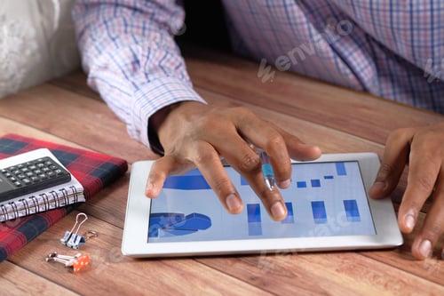 Preview: man's hand working on digital tablet at office desk, using self created chart