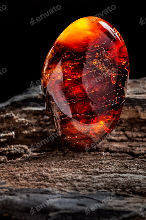 Preview: Natural amber. A piece of dark red semi transparent natural amber on piece of stoned wood