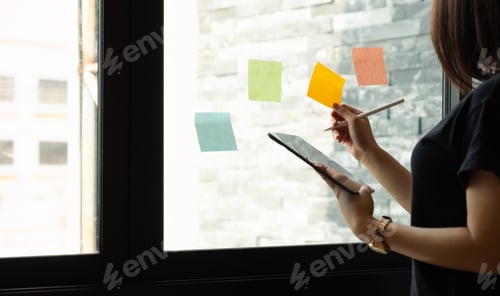 Preview: business woman using tablet during post it notes idea discussing and planning in glass wall at