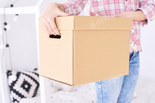 Preview: Person carrying cardboard box in cozy home setting with casual attire