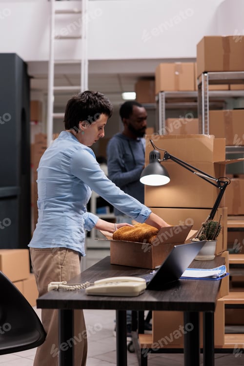 Preview: Warehouse employee putting trendy clothes in carton boxes preparing packages for delivery