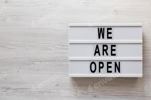Preview: 'We are open' text on a lightbox on a white wooden background, top view.