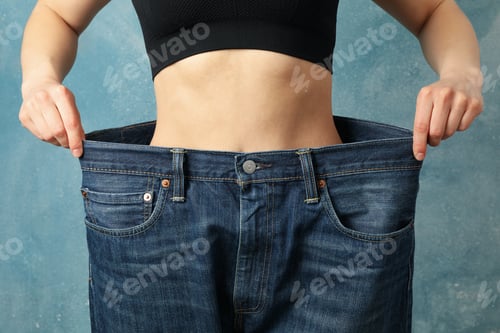 Preview: Girl pulling her big jeans and showing weight loss on blue background