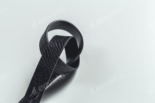 Preview: Black leather belt with a textured design lying on a flat surface in a bright environment