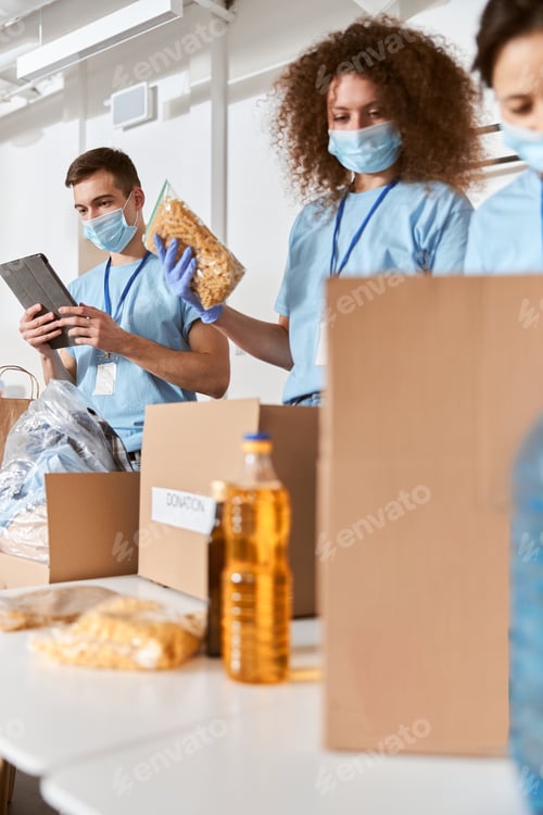 Preview: Group of busy volunteers wearing blue uniform, protective masks and gloves calculating, sorting