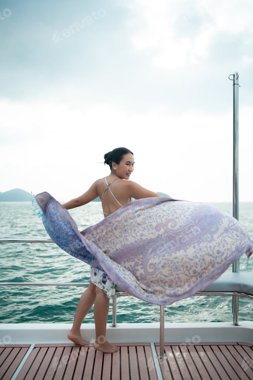 Preview: An Asian girl on a yacht stand to receive the fresh air from the sea with a shawl that flew