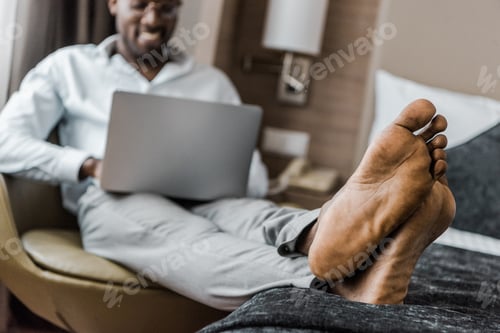 Preview: selective focus of barefoot african american man using laptop in hotel room