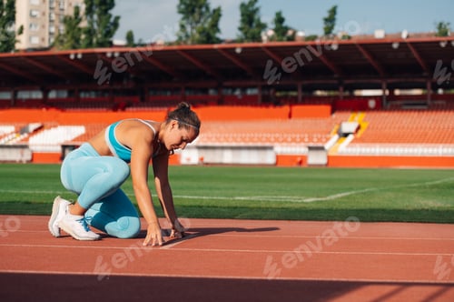 Preview: A sportswoman kneeling in start position on running track on stadium.