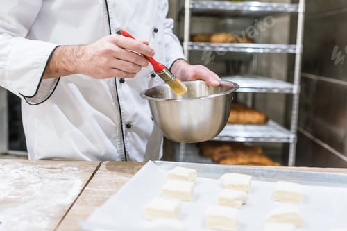 Preview: close up of baker hands oiling dough pieces with basting brush
