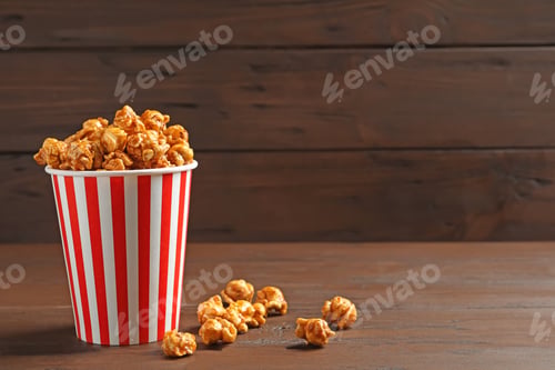 Preview: Delicious popcorn with caramel in paper bucket on wooden table against dark background