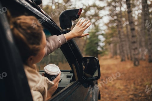 Preview: Millennial woman travelling off-road by car in a forest, drinking coffee, enjoying wind.