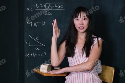 Preview: Young asian woman pretending to be a child raise her hand in math class.