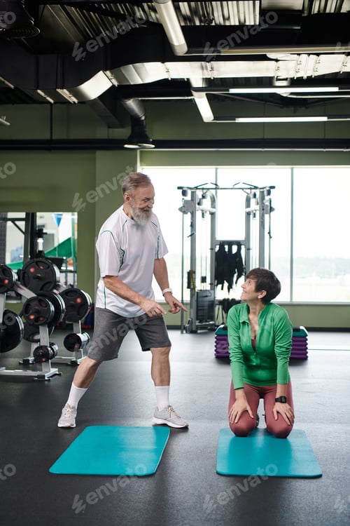 Preview: happy elderly couple near fitness mats, looking at each other, full length, active seniors, sporty