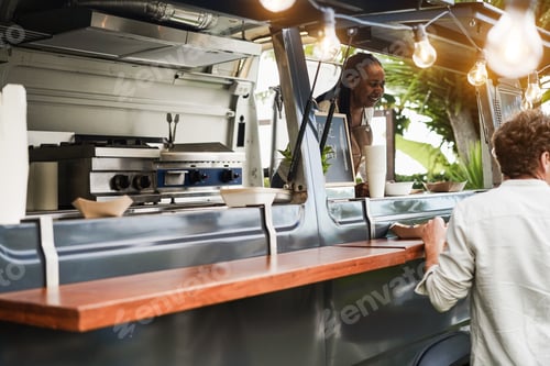 Preview: African senior woman serving take away food inside food truck - Focus on man food box