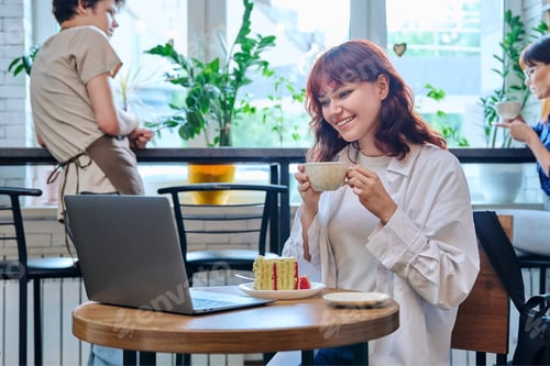 Preview: Female college student with laptop in cafe, with cup of coffee, piece of cake