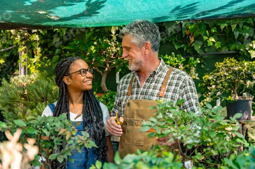 Preview: Master gardener teaching schoolgirl flower nursery in greenhouse smiling