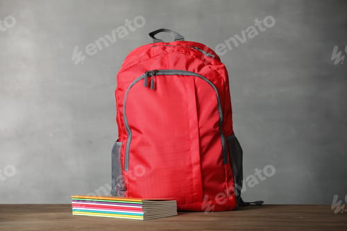 Preview: Red backpack and notebooks on wooden table against gray background. Space for text