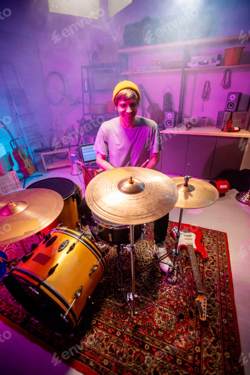 Preview: Cheerful young man sitting by drumset in his garage and going to have rehearsal